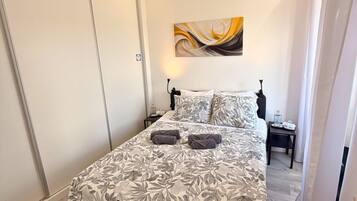 Un dormitorio con cama, mesita de noche, una obra de arte en la pared y una puerta.