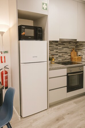 A compact kitchen with a white refrigerator, a microwave, a small oven, and a tiled backsplash.