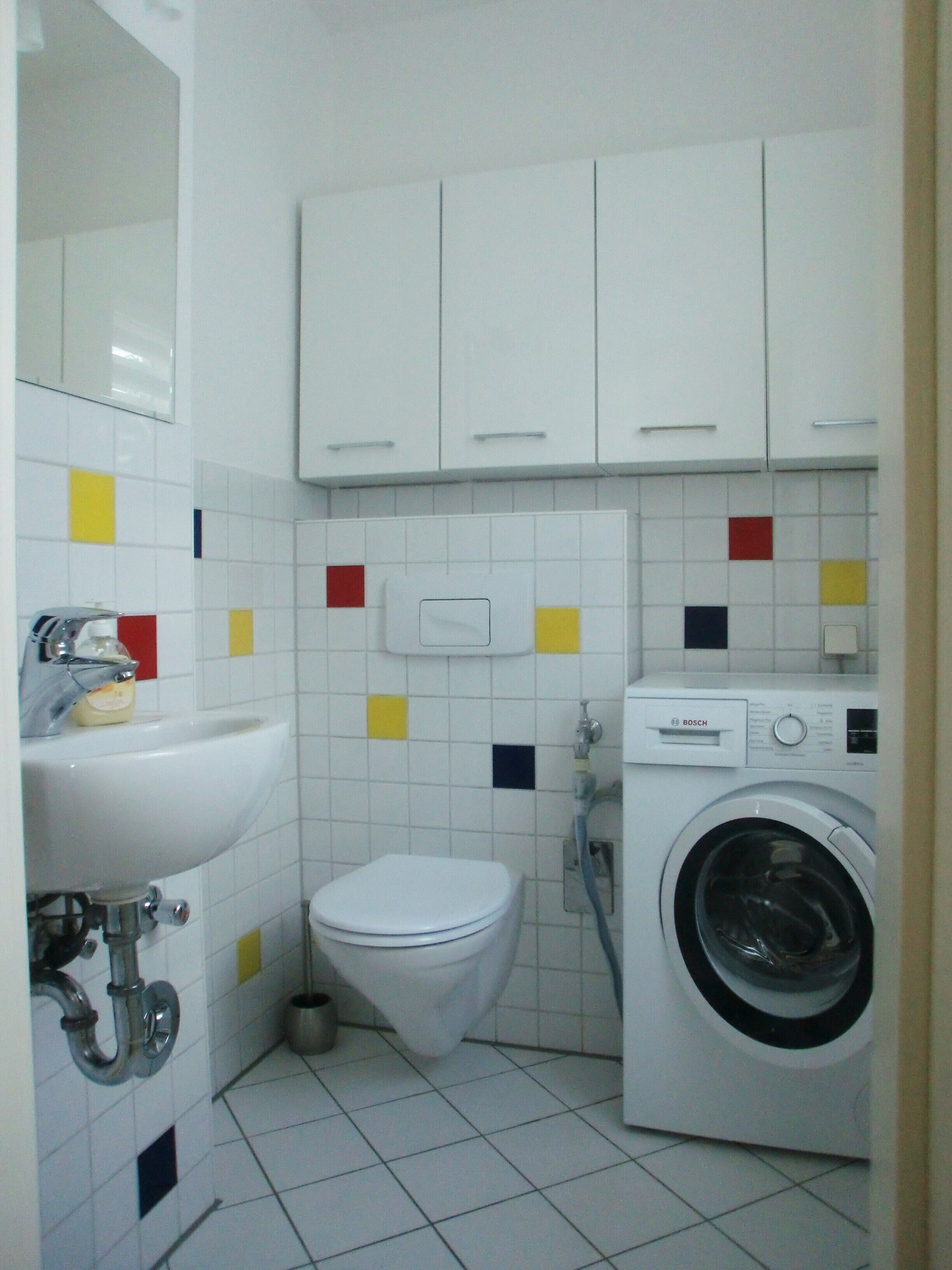Une petite salle de bain compacte, équipée de toilettes, d’un lavabo et d’un lave-linge.