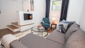 A living room with a sofa, a coffee table, a chair, a TV, and a lamp. - Stylish 1BR oasis with AC, laundry, next to park! (Washington)