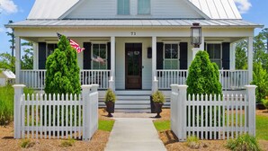 A two-story house with a white facade, a front porch with a white picket fence, and a number '71' on the front door.