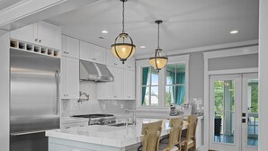 A modern kitchen with a stainless steel refrigerator, a gas stove, and wooden chairs around a central island.