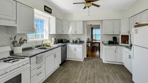 Une cuisine avec des armoires blanches, une cuisinière à gaz, un ventilateur de plafond et une fenêtre donnant sur l’extérieur.