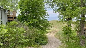 Un chemin de gravier mène à une structure en bois entourée d’une végétation luxuriante.