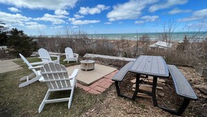 Une terrasse extérieure avec des fauteuils Adirondack, une table ronde et une vue sur l’océan.