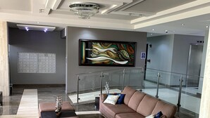 A modern lobby with a brown sofa, a glass railing, and a large abstract painting on the wall. - This is a relaxing18th floor front beach apartment, with magnificent ocean view (Carolina)