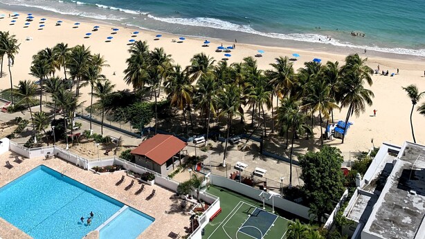 A beach with palm trees, a pool, and a tennis court. - This is a relaxing18th floor front beach apartment, with magnificent ocean view (Carolina)