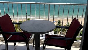 A balcony with a round table and two red chairs, overlooking a beach and the ocean. - This is a relaxing18th floor front beach apartment, with magnificent ocean view (Carolina)