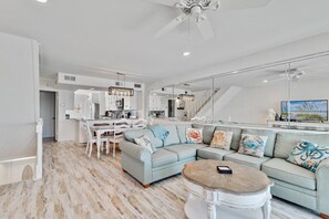A modern living room with a light blue sofa, a wooden coffee table, and a dining area with white furniture.