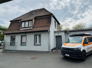 En tvåvåningsbyggnad med ett sluttande tak, en inhägnad gård och en parkerad skåpbil med texten ”Tuning Bus” på.