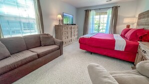 Une chambre à coucher avec un lit rouge, un canapé marron, une commode en bois et un téléviseur posé sur un meuble.