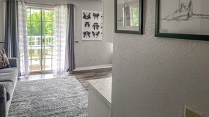 Un salon spacieux avec une grande fenêtre, un canapé gris, une table basse et des œuvres d’art accrochées aux murs.