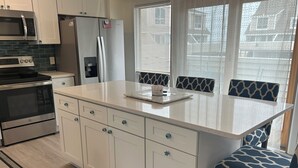 A modern kitchen with white cabinetry, a stainless steel refrigerator, a built-in microwave, and a large island with a sink. - 3 bedroom, 2.5 bath unit - Ocean, bay and pool all in a day! (Lewes)