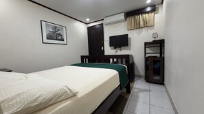 Un dormitorio con cama, televisor, aire acondicionado, armario y un cuadro en la pared.