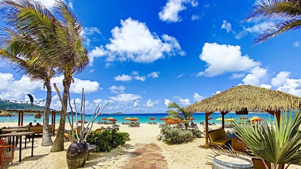 A beachside walkway leading to a beach area with umbrellas, lounge chairs, and a thatched-roof structure. - Villa Cazou, vue mer, piscine privée, Wifi 100Mbps (Oyster Pond)