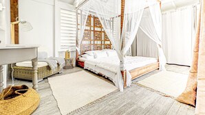 A bedroom with a four-poster canopy bed, a bedside table, a lamp, a wicker chair, and a large woven rug. - Villa Cazou, vue mer, piscine privée, Wifi 100Mbps (Oyster Pond)
