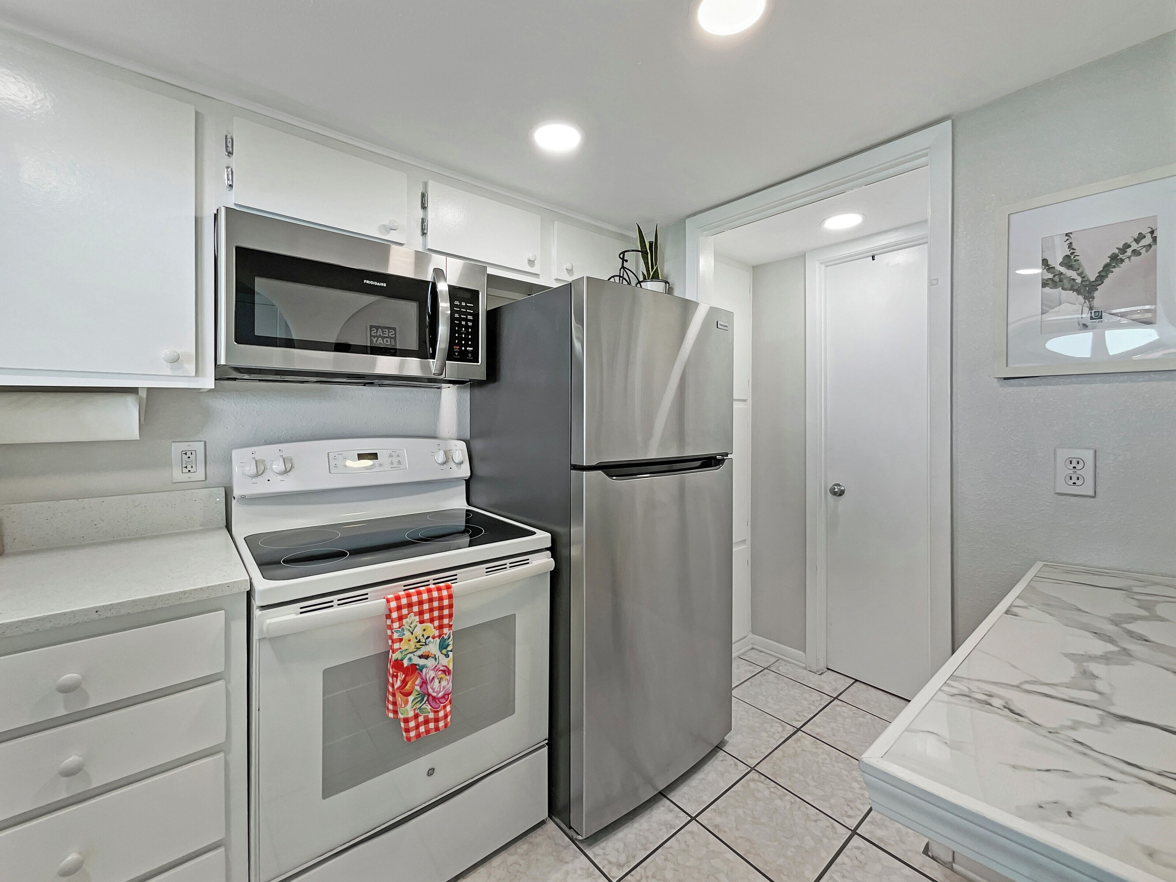 Una cocina moderna con armarios blancos, un refrigerador de acero inoxidable, un microondas y un horno.