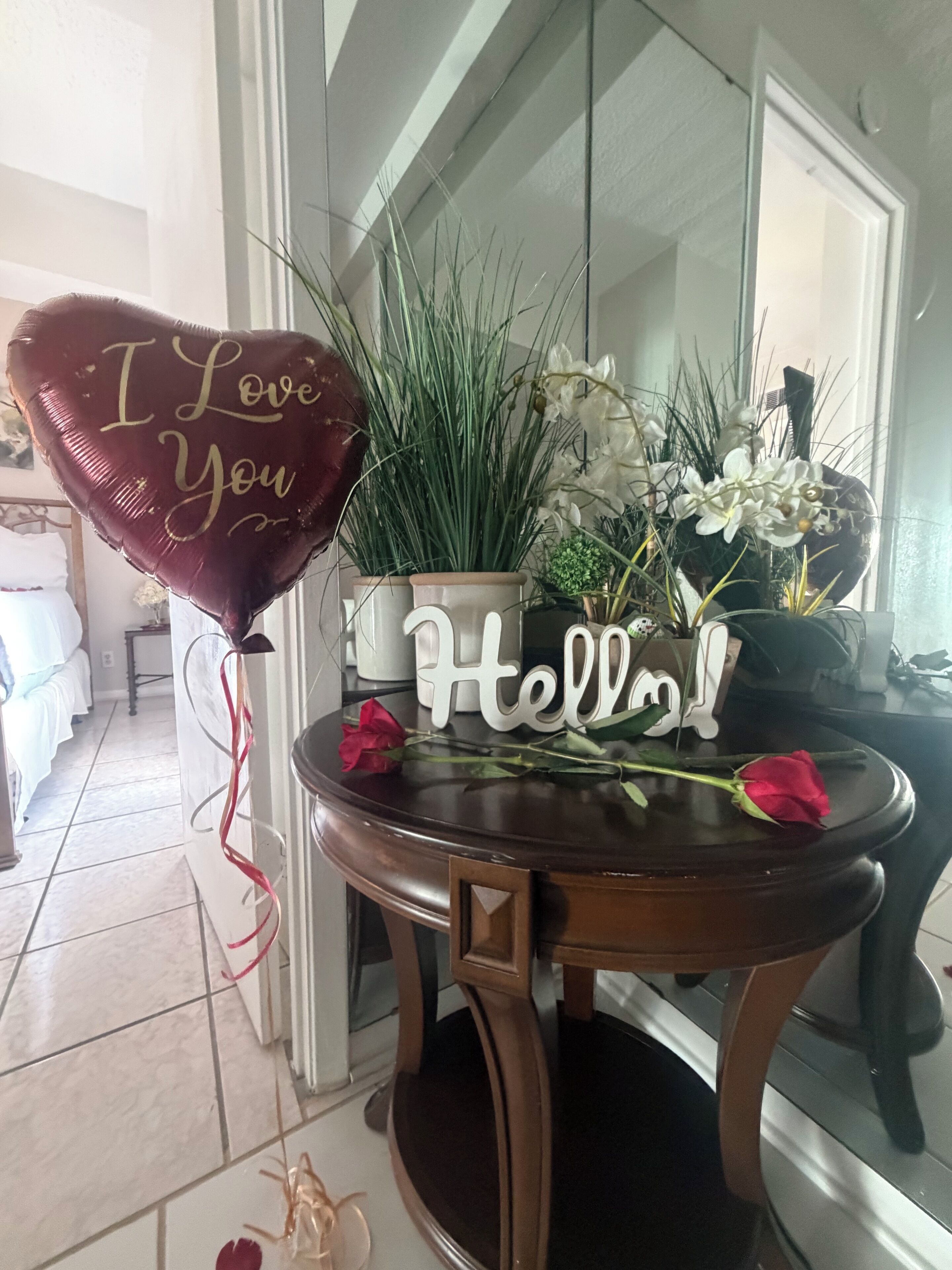 A table with a decorative arrangement including a heart-shaped balloon, a welcome sign, and a bouquet of flowers.