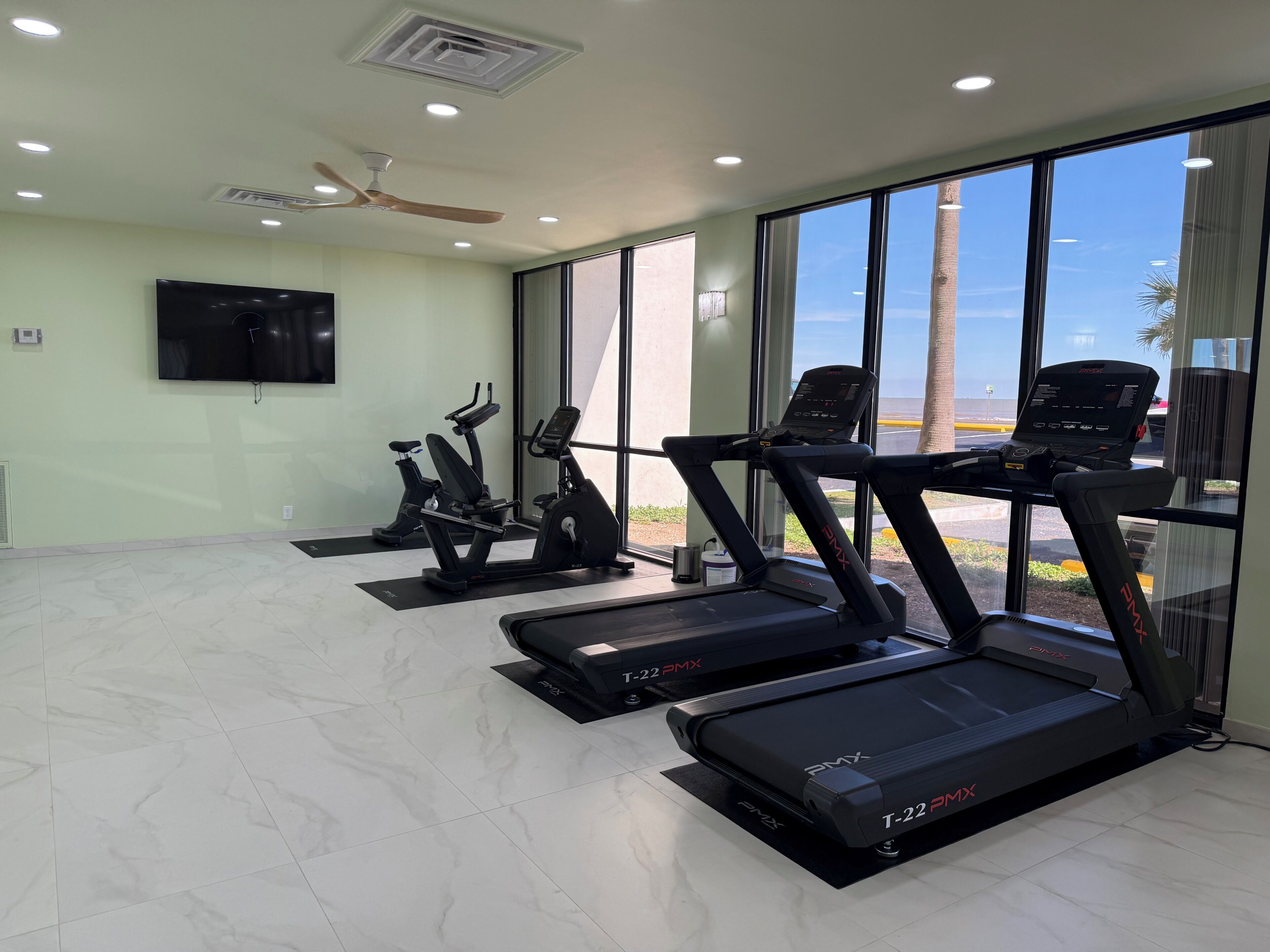 Ein Fitnessstudio mit Laufbändern, Ergometer und einem Deckenventilator.