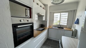 A compact kitchen with a built-in oven, a sink, and a window providing natural light. - Appartement Climatisé Bord de mer Refait a Neuf (Cagnes-sur-Mer)