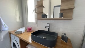 A modern bathroom with a wooden vanity, a black sink, a built-in washing machine, and a mirror above the sink. - Appartement Climatisé Bord de mer Refait a Neuf (Cagnes-sur-Mer)