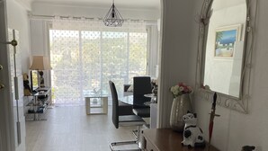 A spacious living area with a wooden dresser, a mirror with a picture, and a dining area with a table and chairs. - Appartement Climatisé Bord de mer Refait a Neuf (Cagnes-sur-Mer)