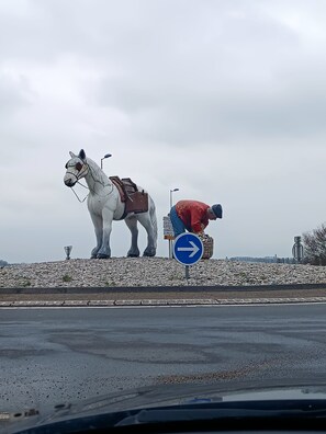 A white horse statue with a saddle and a person in a red jacket bending over a basket.