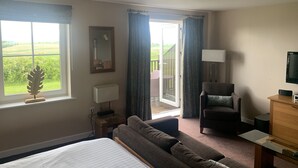 A hotel room with a bed, a sofa, a chair, a desk, a lamp, a TV, and a large window with a view of the outdoors. - Luxury apartment in Whitbarrow Holiday Village near Pooley Bridge & Ullswater (Penrith)
