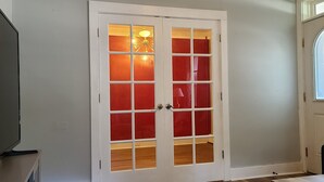 Una habitación con una puerta blanca y paneles de vidrio rojo, una silla negra y una pared blanca con un ventanal pequeño.