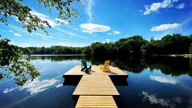 Un muelle de madera que se adentra en aguas tranquilas, con dos sillas encima.