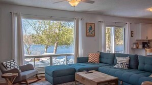 Una sala de estar con sofá, sillón mecedora, mesa de centro y vista al exterior.