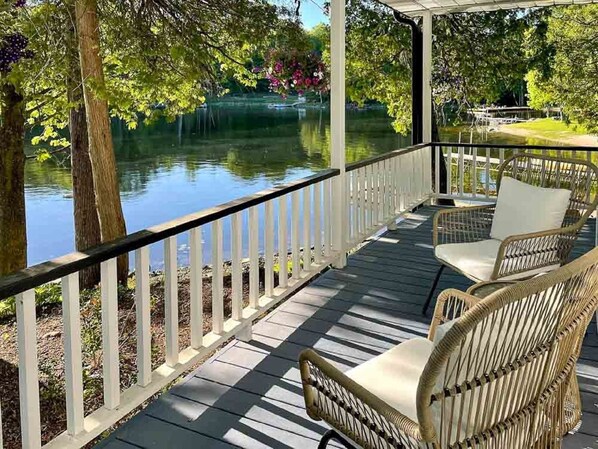 A covered deck with white railings, wicker furniture, and a view of a lake. - Hambly House - Three Bedroom Cottage, Sleeps 6 (Hartington)