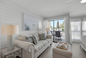 Relax in this inviting living room with a sofa, coffee table, and side table, featuring a large window with a balcony view.