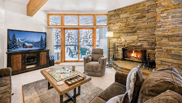 A cozy living room with a stone fireplace, a television, and a large window overlooking a snowy landscape. - Powder Run 12C 100 yards to Lift Unbeatable (Park City)