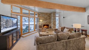 A cozy living room with a stone fireplace, a large TV, and a view of a snowy landscape through large windows. - Powder Run 12C 100 yards to Lift Unbeatable (Park City)