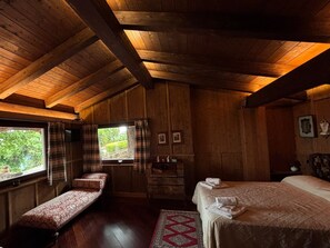 Interno di una baita di legno con un letto, una panca e una finestra con tende.