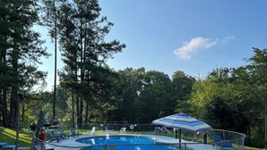 A fenced swimming pool with a deck area, surrounded by trees and outdoor furniture. - Rustic Bee Cabin - camping (Hardin)