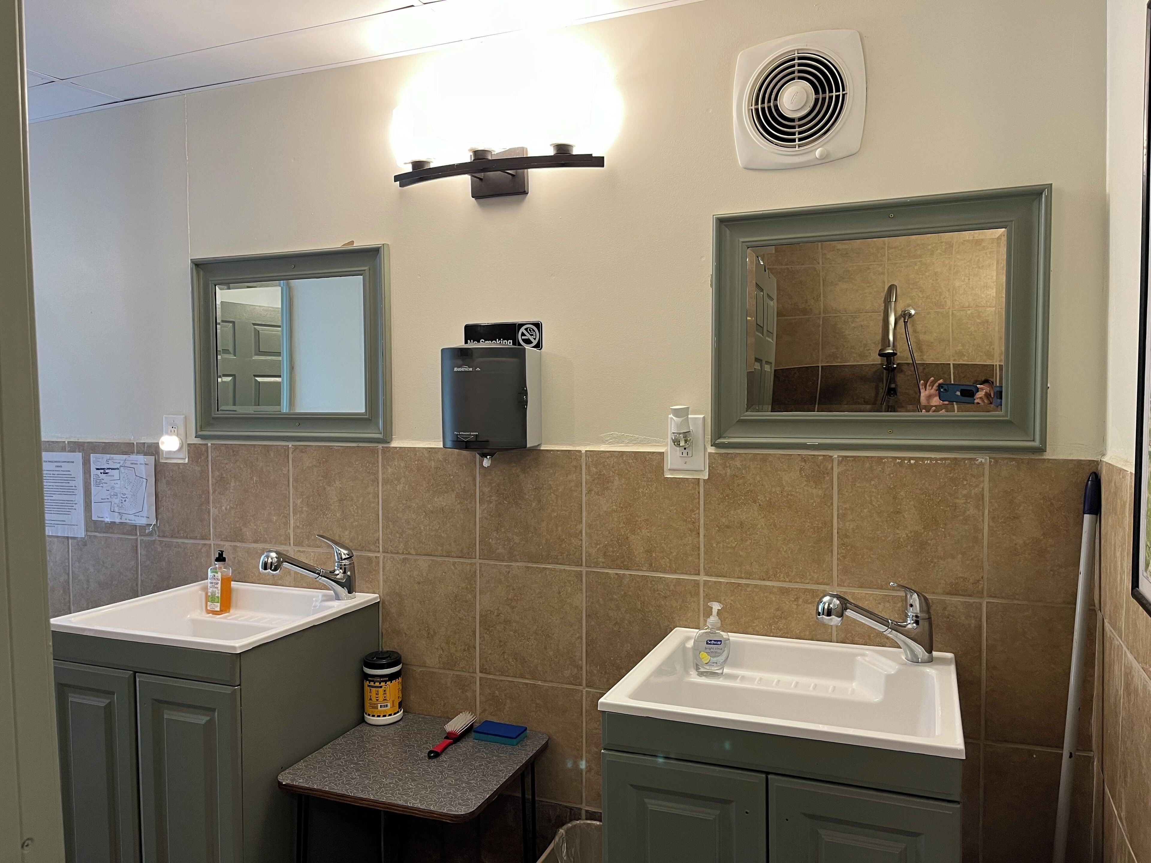 Un baño con dos lavamanos, un espejo, un secador de manos y un ventilador de pared.