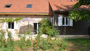 Una casa con fachada de piedra, techo de tejas y un jardín con plantas de tomate.