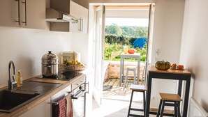 Una cocina con lavaplatos, estufa y vistas a un jardín por una puerta abierta.