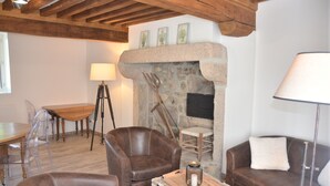 Un salón acogedor con chimenea de piedra, sillones de cuero, una mesa de comedor de madera y sillas de plástico transparente.