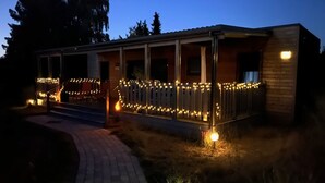 Een gebouw met een veranda versierd met lichtslingers, een met baksteen bestraaide oprit en een houten hek.