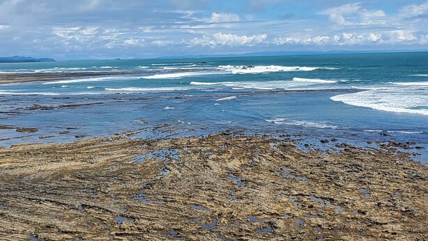 A coastal landscape with a rocky shoreline and waves.