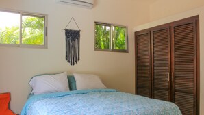 A bedroom with a bed, two windows, a wall hanging, and a closet.