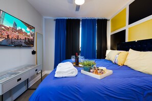 Hotellihuone, jossa on suuri sänky, seinälle asennettu taulutelevisio, yöpöytä ja ikkuna, jossa on verhot.