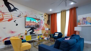 A modern living room with a large TV, comfortable seating, and a cityscape artwork on the wall. - The Six1five by Extremely Suite★4 beds/4baths★9 BEDS★ROOFTOPDECK★HUGE SPACE (Nashville)