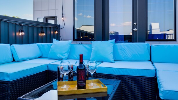 A rooftop seating area with a blue sofa, a tray with wine glasses and a bottle, and a city view through large windows. - The Six1five by Extremely Suite★4 beds/4baths★9 BEDS★ROOFTOPDECK★HUGE SPACE (Nashville)