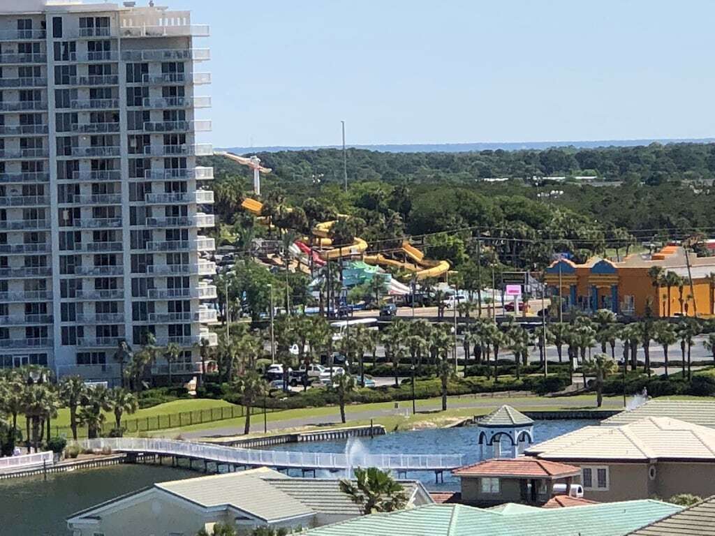 Un hotel di grattacielo con numerosi balconi, un parco acquatico con scivoli e piscina, e un ponte sopra un corso d'acqua.