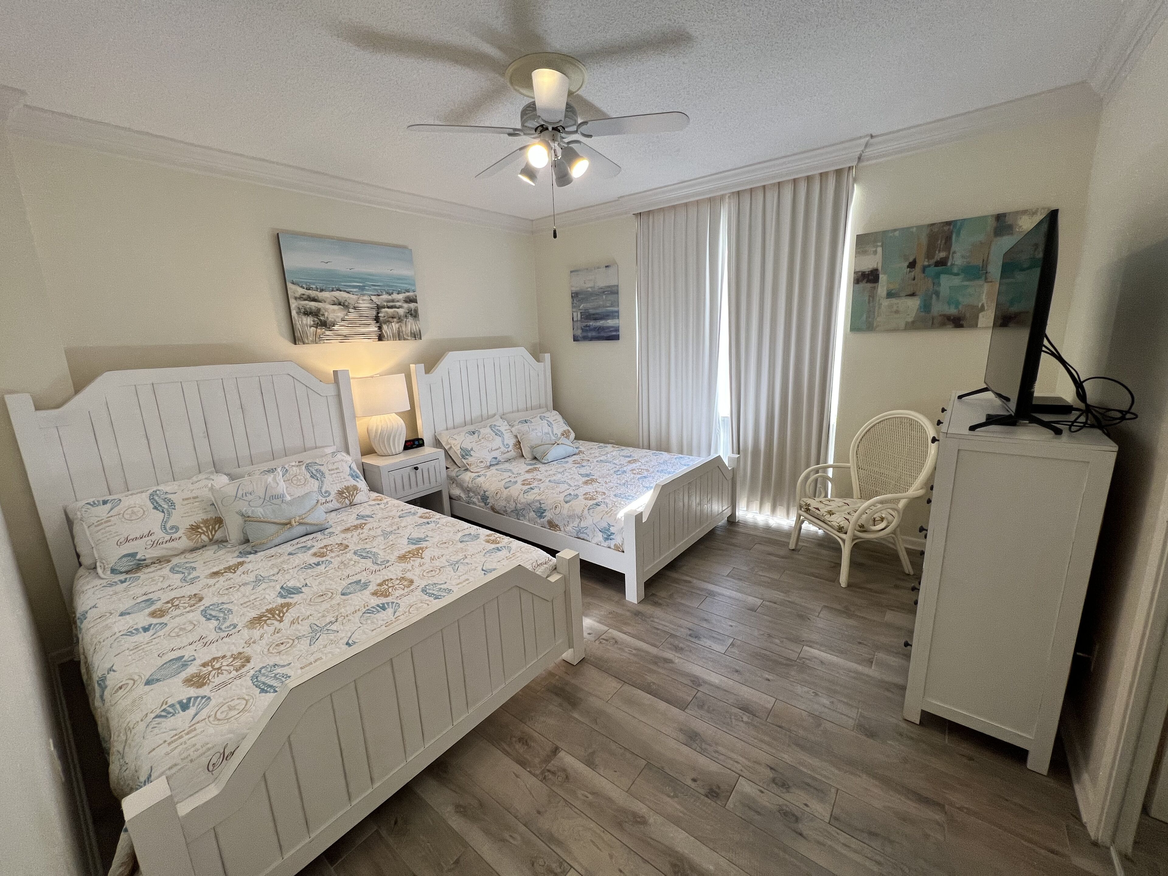 A room with two single beds, a ceiling fan, a desk with a computer, a chair, and a cabinet.