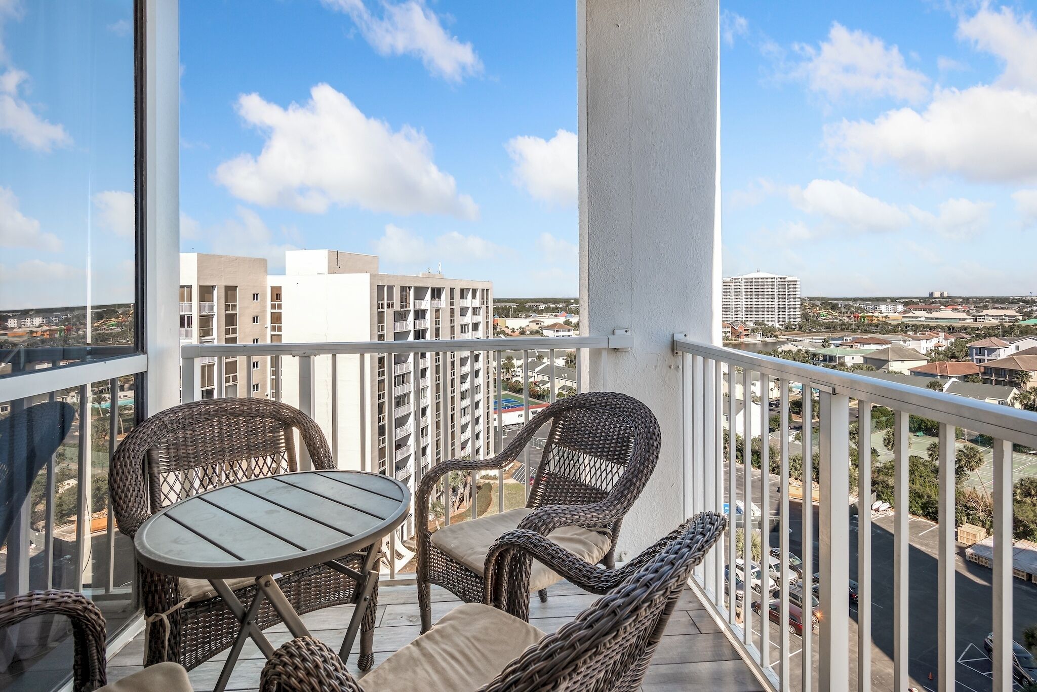 A balcony with wicker furniture, a table, and a view of surrounding buildings.